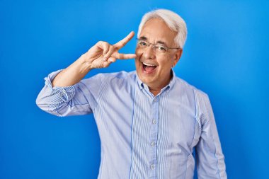 İspanyol kıdemli gözlüklü, barış sembolü takan, yüzünde parmakları olan, gülümseyen, zafer gösteren bir adam. 