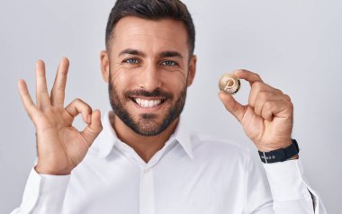 Yakışıklı İspanyol adam elinde polkadot kripto para tutuyor. Parmaklarıyla imza atıyor, gülümsüyor. Mükemmel bir sembol. 