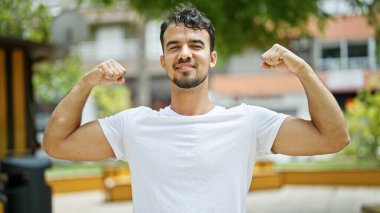 Genç İspanyol gülümseyen adam parkta güçlü hareketler yapıyor.