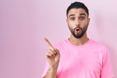 Pembe arka planda dikilen Latin kökenli genç adam parmağını yana çevirerek şaşırdı, ağzı açık hayret içinde kaldı.. 