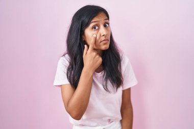 Young hispanic woman standing over pink background pointing to the eye watching you gesture, suspicious expression 