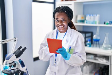 African american woman scientist smiling confident using touchpad at laboratory