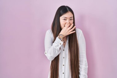 Pembe arka planda duran Çinli genç bir kadın pis ve iğrenç bir koku alıyor. Nefesini burnunda tutuyor. Kötü kokuyor. 