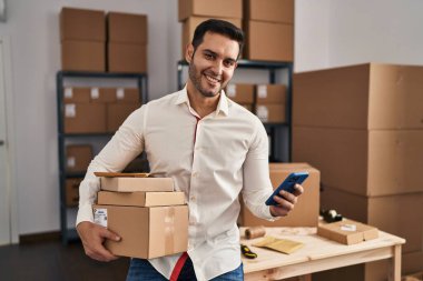 Genç İspanyol bir e-ticaret işçisi ofisteki akıllı telefon paketlerini kullanıyor.