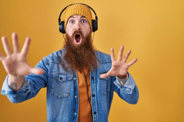 Uzun sakallı, müzik dinleyen, kulaklık takan, korkudan dehşete düşmüş beyaz bir adam. El kol hareketi yapmayı kes, şok içinde bağır. panik konsepti. 
