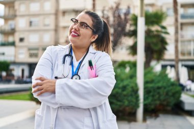 Genç, güzel, iri yarı bir kadın doktor gülümsüyor. Parkta kollarını kavuşturmuş duruyor.