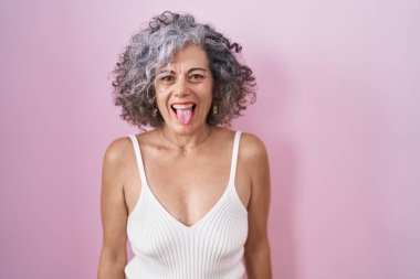 Pembe arka planda duran gri saçlı orta yaşlı kadın komik bir ifadeyle dilini dışarı çıkartıyor. duygu kavramı. 