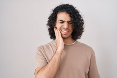 Hispanic man with curly hair standing over white background touching mouth with hand with painful expression because of toothache or dental illness on teeth. dentist  clipart