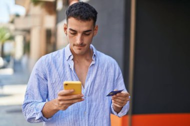 Genç İspanyol adam akıllı telefon ve kredi kartı kullanıyor.