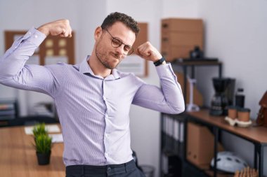 Ofisteki genç İspanyol adam gururla gülümseyen kol kaslarını gösteriyor. fitness konsepti. 