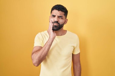 Sarı arka planda duran İspanyol sakallı adam diş ağrısı ya da diş hastalığından dolayı acı dolu bir ifadeyle ağıza dokunuyor. dişçi 