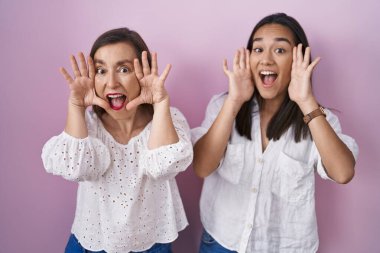 Hispanic mother and daughter together smiling cheerful playing peek a boo with hands showing face. surprised and exited 