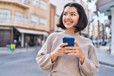 Sokakta akıllı telefon kullanan kendine güvenen genç bir kadın.