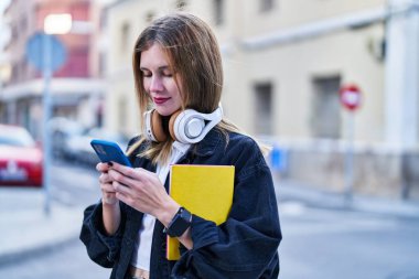 Sokakta akıllı telefon kullanan genç sarışın kız öğrenci.