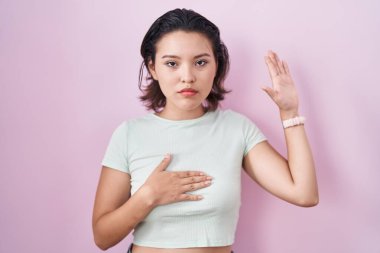 Latin kökenli genç bir kadın pembe arka planda el pençe divan durup, el pençe divan durarak sadakat yemini ediyor. 
