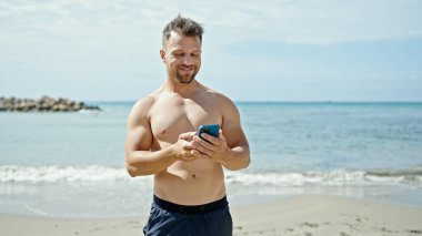 Kumsalda gülümseyen akıllı telefon kullanan genç bir turist.