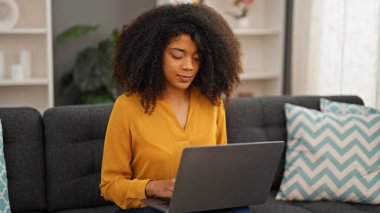 African american woman using laptop sitting on sofa at home