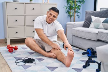 Genç latin adam gülümsüyor evde kendine güvenen esneme bacağı