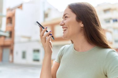 Genç, güzel bir kadın, gülümsüyor. Kendine güveniyor. Akıllı telefondan konuşuyor.