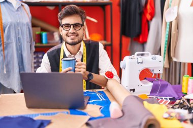 Genç İspanyol terzi atölyede kahve içerken dizüstü bilgisayar kullanıyor.