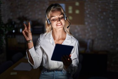 Geceleri ofiste çalışan genç sarışın kadın kameraya bakıp zafer işareti yaparken gülümsüyor. İki numara.. 