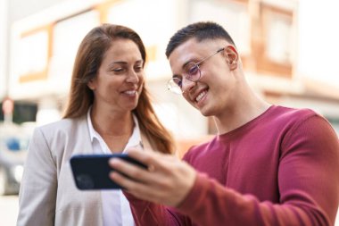 Man and woman mother and son smiling confident using smartphone at street