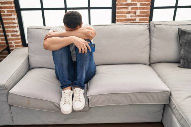 Young hispanic man stressed sitting on sofa at home