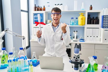 Laboratuvarda çalışan Latin asıllı genç adam diplomasını tutuyor. Gururla bağırıyor, zaferi ve başarıyı kutluyor. Kollarını kaldırıp heyecanla bekliyor. 