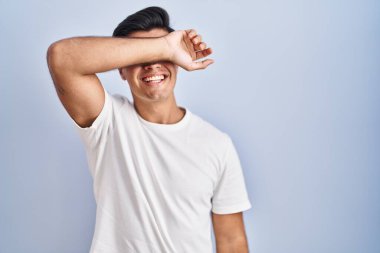 Mavi arka planda dikilen İspanyol adam kollarıyla gözlerini kapatıyor neşeli ve komik gülümsüyor. kör kavram. 