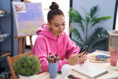 Sanat stüdyosunda akıllı telefon kullanarak kendine güvenen genç bir sanatçı.