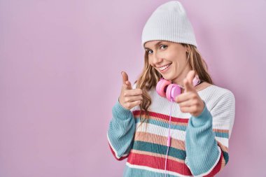 Young blonde woman standing over pink background pointing fingers to camera with happy and funny face. good energy and vibes. 