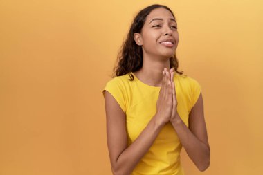 Genç Afro-Amerikalı kadın, izole edilmiş sarı arka planda ellerini birleştirip özür diliyor.