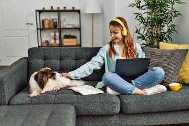 Kanepede oturan beyaz bir kadın ve evde ders çalışan bir köpek.