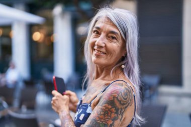 Middle age grey-haired woman smiling confident using smartphone at street