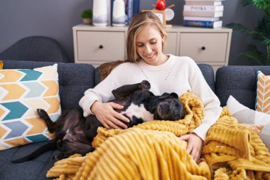 Young blonde woman hugging dog sitting on sofa at home