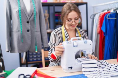 Terzide dikiş makinesi kullanan kendine güvenen genç sarışın kadın terzi.