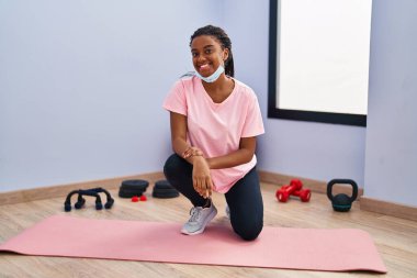 Spor kıyafetleri ve güvenlik maskesi takan Afrikalı genç bir Amerikalı spor salonunda pozitif ve mutlu görünüyor ve gülümseyerek dişlerini gösteriyor. 