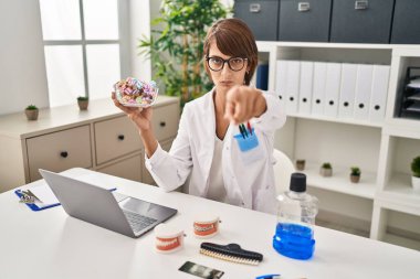 Esmer dişçi kadın kamerayı işaret eden şekerlemeler tutuyor ve sen kendine güvenen ciddi bir jest yapıyorsun. 