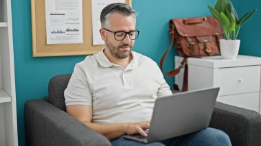 Ofiste çalışan beyaz saçlı bir iş adamı dizüstü bilgisayar kullanıyor.