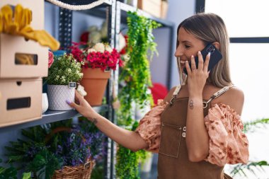 Çiçekçide elinde saksıyla akıllı telefondan konuşan güzel İspanyol kadın.