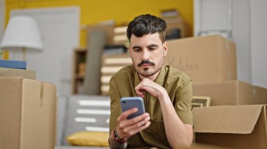 Genç İspanyol adam yeni evinde akıllı telefon kullanıyor.