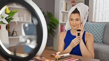 Genç, güzel, İspanyol bir kadın gülümsüyor. Evde kendine güvenen bir makyaj dersi veriyor.