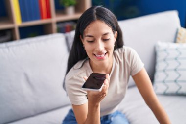 Evdeki kanepede oturmuş akıllı telefondan konuşan genç, güzel İspanyol kadın.