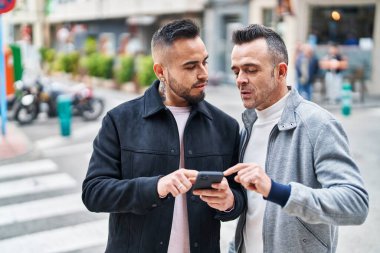 İki erkek caddede rahat bir ifadeyle akıllı telefon kullanıyor.