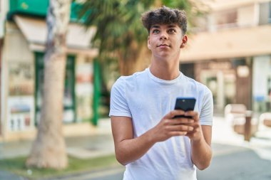 Young hispanic teenager smiling confident using smartphone at street