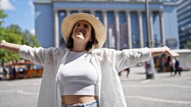 Güzel, genç İspanyol bir kadın, kendine güvenen, yaz şapkalı, kolları açık Nobel ödüllü bir binada duruyor.