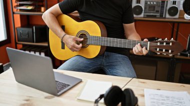 Genç İspanyol müzisyen müzik stüdyosunda dizüstü bilgisayar kullanarak klasik gitar çalıyor.