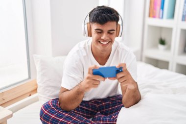 Genç İspanyol adam gülümsüyor. Yatak odasında oyun oynarken kendine güveniyor.