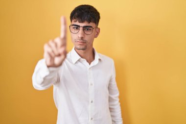 Sarı arka planda dikilen genç İspanyol adam parmağını kaldırmış ve kızgın bir ifadeyle işaret ediyor, hiçbir hareket göstermiyor. 