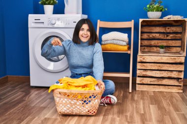 Çamaşır odasında elini ve parmağını göstererek mutlu bir şekilde gülümseyen genç İspanyol kadın. 